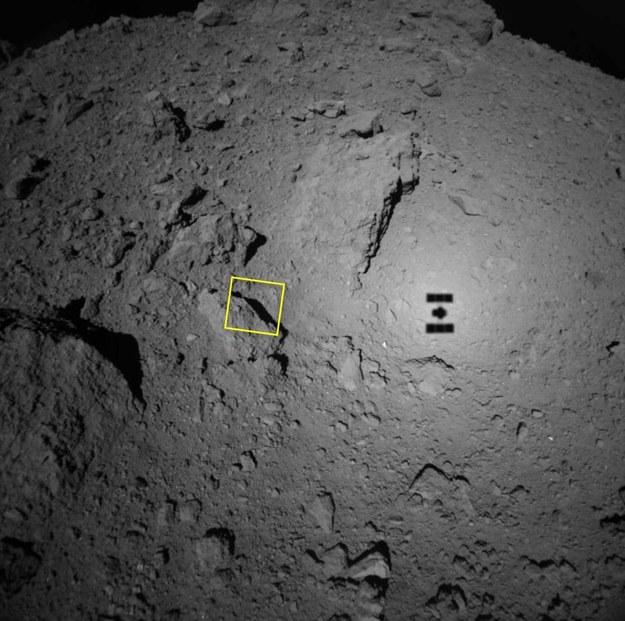 Cień sondy Hayabusa 2 na tle planetoidy Ryugu (żółtym kwadratem oznaczono obszar widoczny na zdjęciu z kamery ONC-T /JAXA, University of Tokyo, Kochi University, Rikkyo University, Nagoya University, Chiba Institute of Technology, Meiji University, Aizu University, AIST /Materiały prasowe