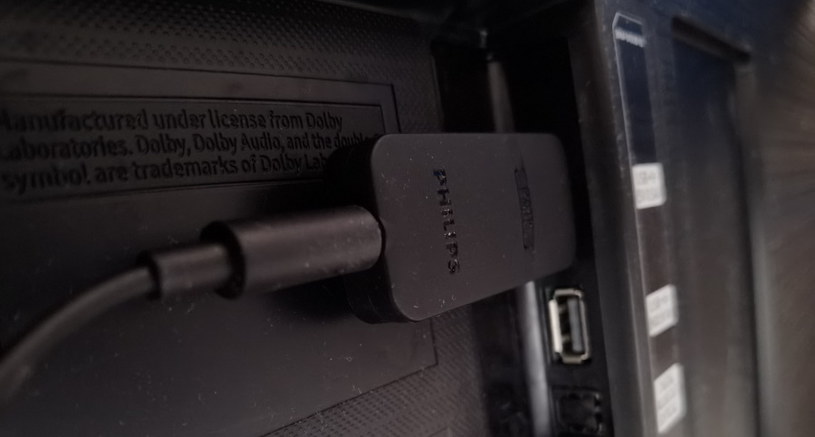 Dongle (nadajnik) umieszczony w porcie USB w telewizorze (odbiornik dostarcza zasilanie), a z pomocą kabela 3,5 mm podłączonego do wyjścia słuchawkowego 3,5 mm, nadajnik odbiera sygnał audio i przesyła do słuchawek /INTERIA.PL