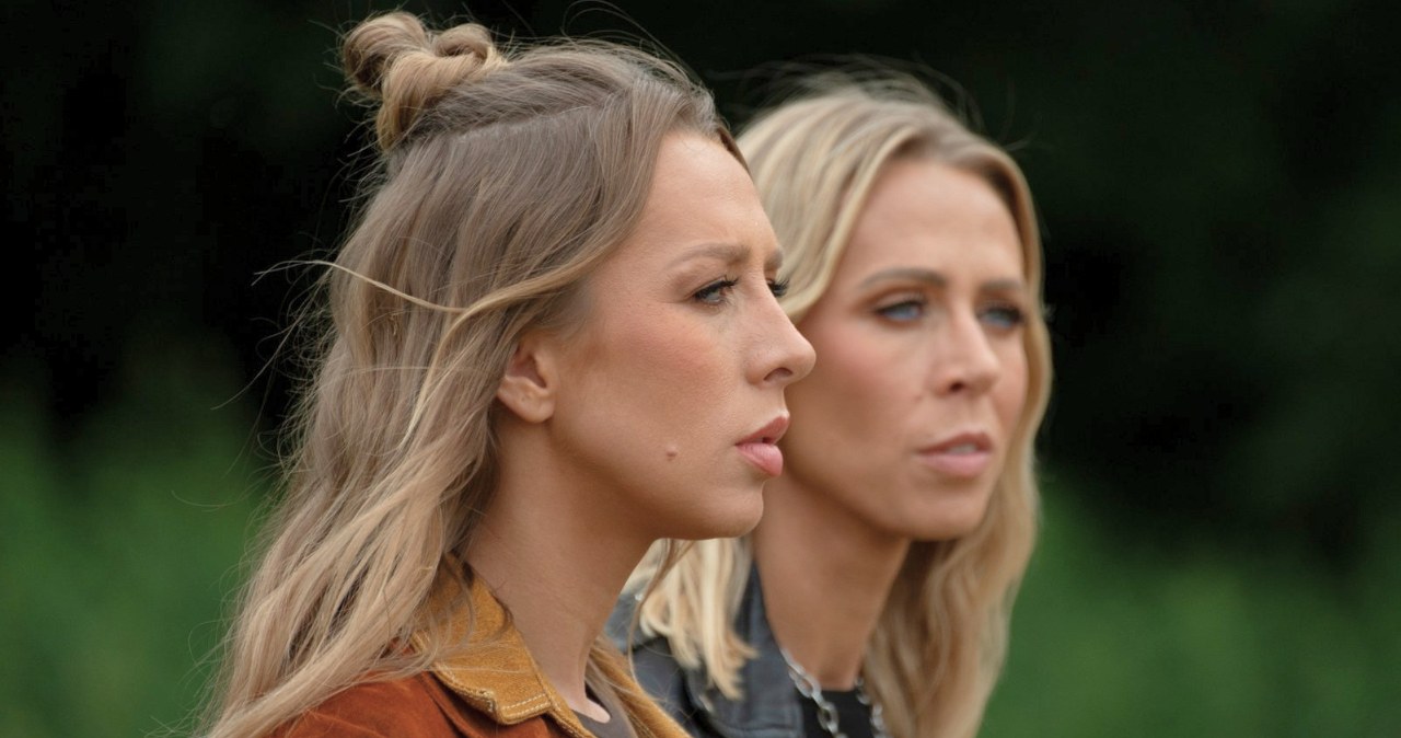 Dwie kobiety o blond włosach stoją obok siebie, patrząc w jednym kierunku z poważnym wyrazem twarzy, na tle rozmytej zieleni. /Polsat /materiały promocyjne