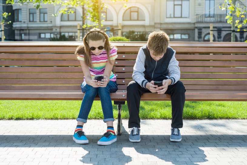 Dzieci na ławce ze smartfonami /Adobe Stock