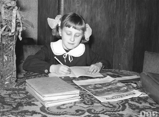 Dziewczynka odrabia lekcje przy stole. Widoczne książki i egzemplarz pisma "Świerszczyk" /Z archiwum Narodowego Archiwum Cyfrowego