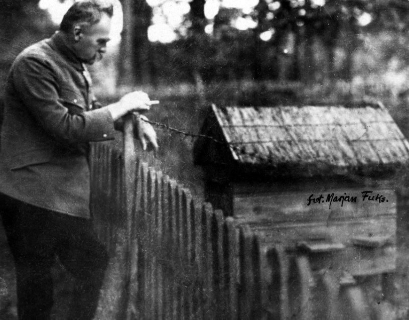 Józef Piłsudski pali papierosa oparty o płot i obserwuje ul w Sulejówku /Z archiwum Narodowego Archiwum Cyfrowego