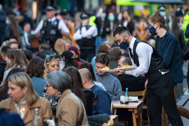Kelnerzy obsługują ludzi przy stolikach na zewnątrz w centrum Londynu, po złagodzeniu obostrzeń na Wyspach /Dominic Lipinski   /PAP/EPA