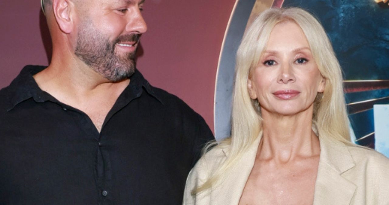 Kobieta o długich blond włosach w jasnej marynarce stoi obok mężczyzny w ciemnej koszuli z ogolonymi włosami, patrzącego w jej stronę, na tle scenerii w odcieniach granatu i bordowego. / Jacek Kurnikowski /AKPA