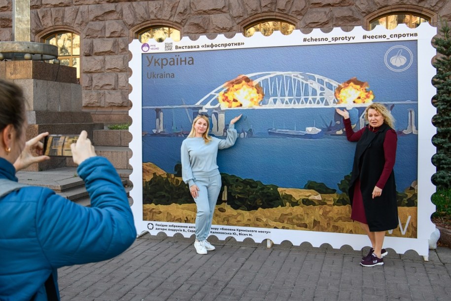 Ludzie pozują na tle wydruku w postaci znaczka pocztowego, przedstawiającego Most Krymski w ogniu (Kijów) /Vladyslav Musiienko
