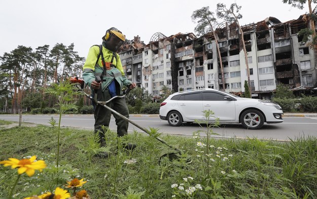 Mężczyzna kosi trawę przed zniszczonym w ostrzale budynkiem w Irpieniu /SERGEY DOLZHENKO /PAP/EPA