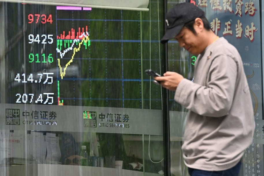 Muž prochází obrazovkou zobrazující burzovní indexy v Pekingu /Adek Berry /AFP /East News