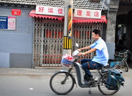 Mieszkaniec Pekinu przejeżdża obok zamkniętego  salonu masażu, 9 lipca 2008 /AFP