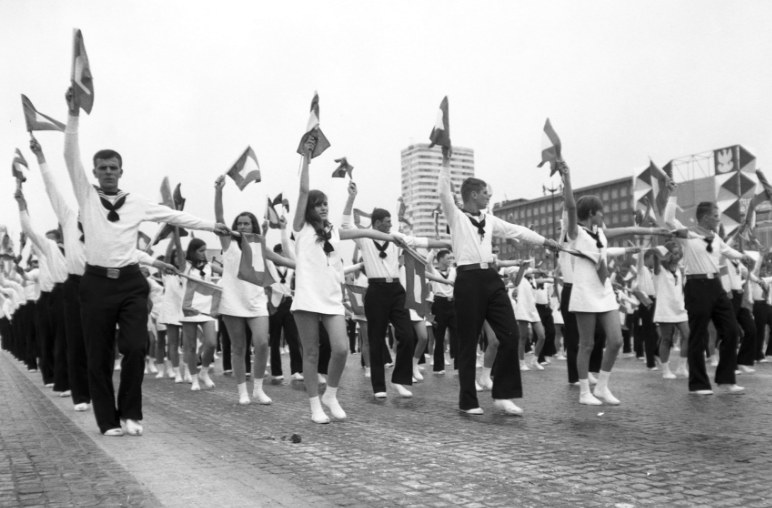 Młodzież wykonująca układy gimnastyczne z chorągiewkami podczas przemarszu ulicą Marszałkowską w Warszawie /Z archiwum Narodowego Archiwum Cyfrowego