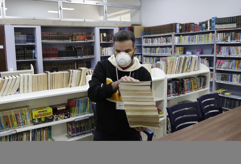 Nauczyciel trzyma stertę książek ze szkolnej biblioteki, która jest dezynfekowana w związku z epidemią koronawirusa. /Hussein Malla /East News