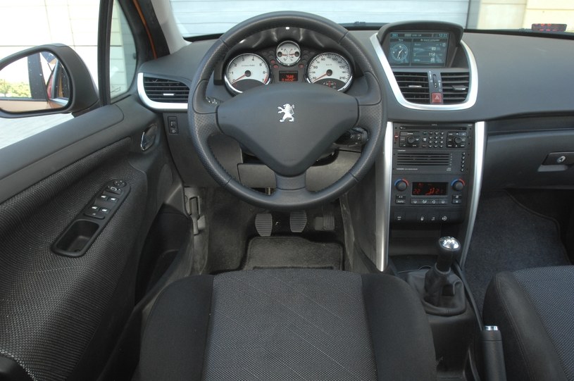 Peugeot 207: w sportowym stylu. Deska rozdzielcza i kierownica są osadzone dość wysoko. Obsługa radioodtwarzacza i klimatyzacji absorbuje uwagę. Białe tarcze zegarów to opcja. /Motor
