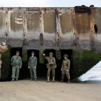   Pasjonaci historii w replikach mundurów wojskowych fotografujący się na tle wraku pontonu