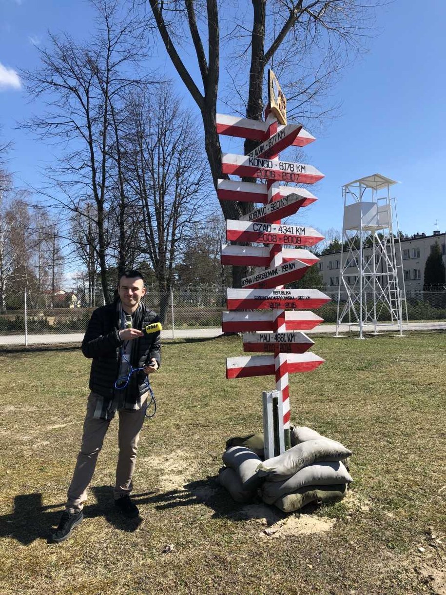Reporter RMF FM Michał Dobrołowicz i drogowskaz pokazujący, jaka odległość dzieli Kielce od najczęstszych miejsc, gdzie polscy żołnierze pracują w ramach misji pokojowych. Najdalej? Kambodża! Ponad 8 tysięcy kilometrów! /Michał Dobrołowicz /RMF FM