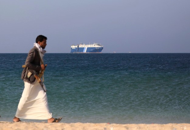 Uzbrojony bojownik Huti w porcie w Jemenie nad Morzem Czerwonym, w tle porwany statek Galaxy Leader. Zdjęcie wykonane 6 grudnia 2023 roku. /YAHYA ARHAB /PAP/EPA