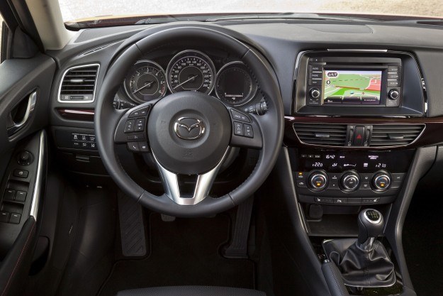 Wysoko zabudowana deska rozdzielcza niewiele różni się od tej z modelu CX-5. W „szóstce" zastosowano jednak więcej eleganckich, lśniących okładzin. Plus za mięsistą kierownicę i przejrzyste zegary z białym podświetleniem, minus za niewielką liczbę schowków. /Mazda