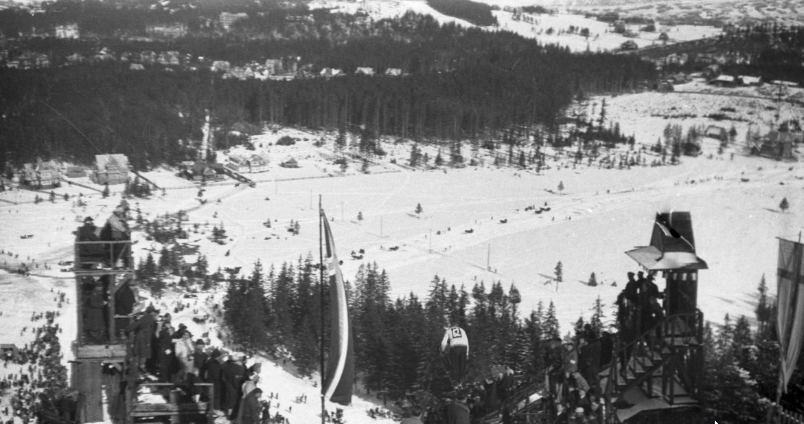 Zawodnik w skoku narciarskim z Wielkiej Skoczni na Krokwi. Po bokach na trybunach widoczni kibice. Zdjęcie z 1935 roku /Z archiwum Narodowego Archiwum Cyfrowego